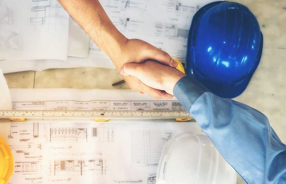 engineers shaking hands over detailed drawings